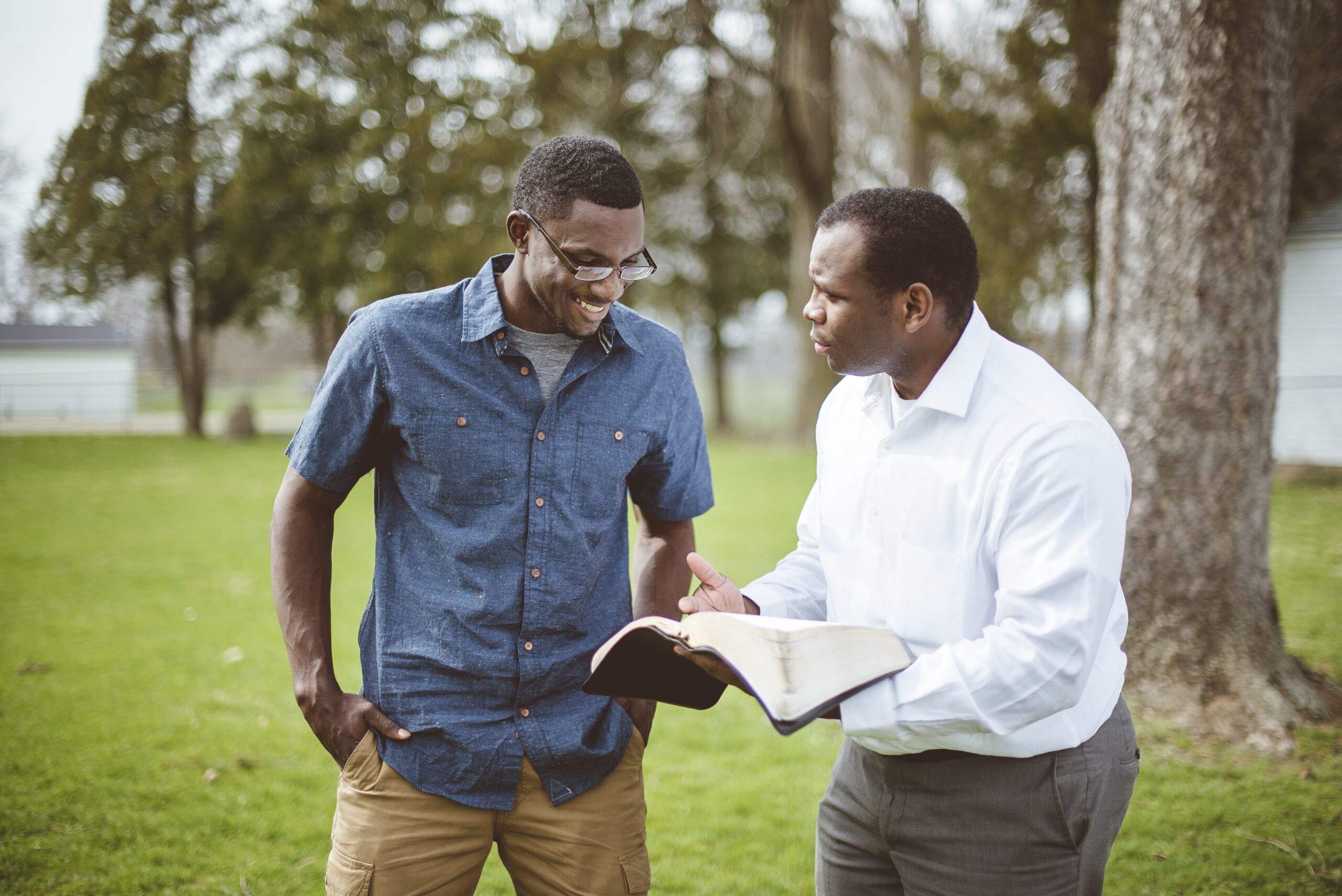 Two African-American male friends standing at the park and discussing the Bible